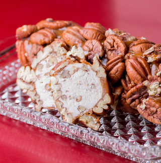 Roll of cream cheese filled with pecans on a decorative glass plate against a red background
