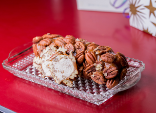 Roll of cream cheese filled with pecans on a decorative glass plate against a red background